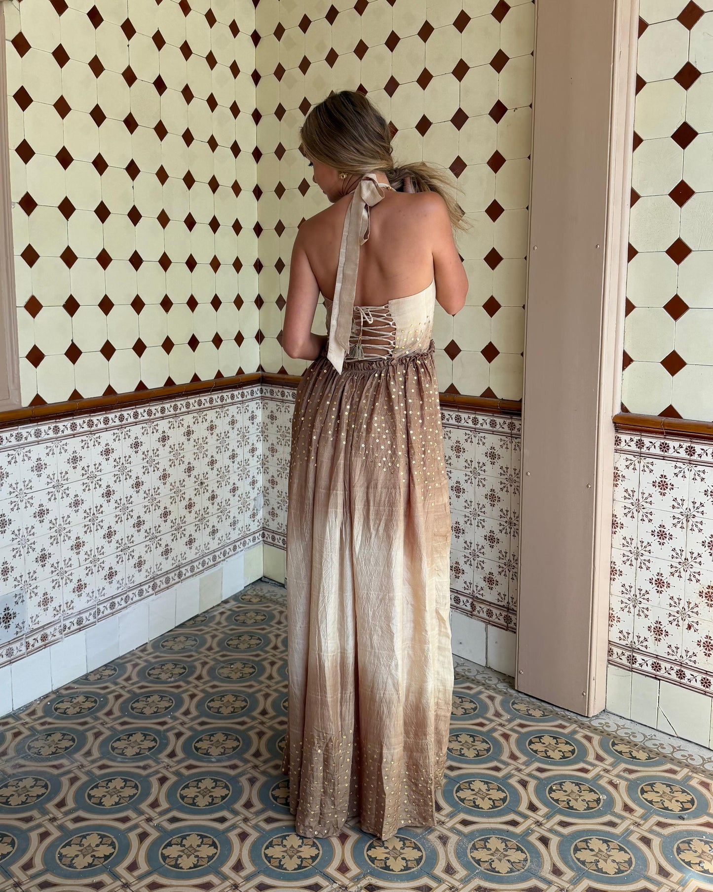 
                  
                    Aarohi Dress in handwoven mulberry silk featuring ivory-to-mocha Shibori dyeing, hand-sewn brass sequins, embroidered bodice, halter tie straps, and a flowing floor-length silhouette.
                  
                