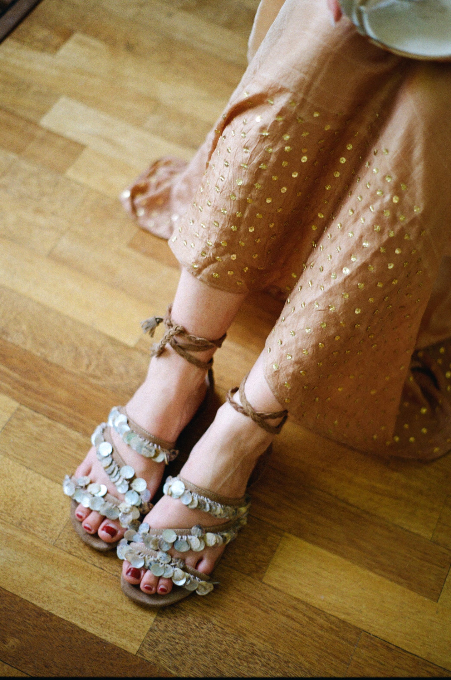 Handcrafted tan suede flat sandals with mother of pearl beads and braided wrap-around ankle ties.