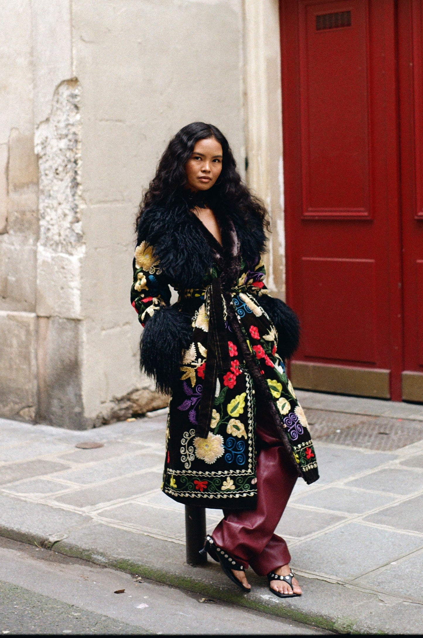 One-of-a-kind ZAZI Afghan coat crafted from vintage velours cotton suzani embroidery with an up-cycled sheepskin lining, featuring a belted 1970s Penny Lane silhouette and handcrafted by women artisans in Afghanistan.