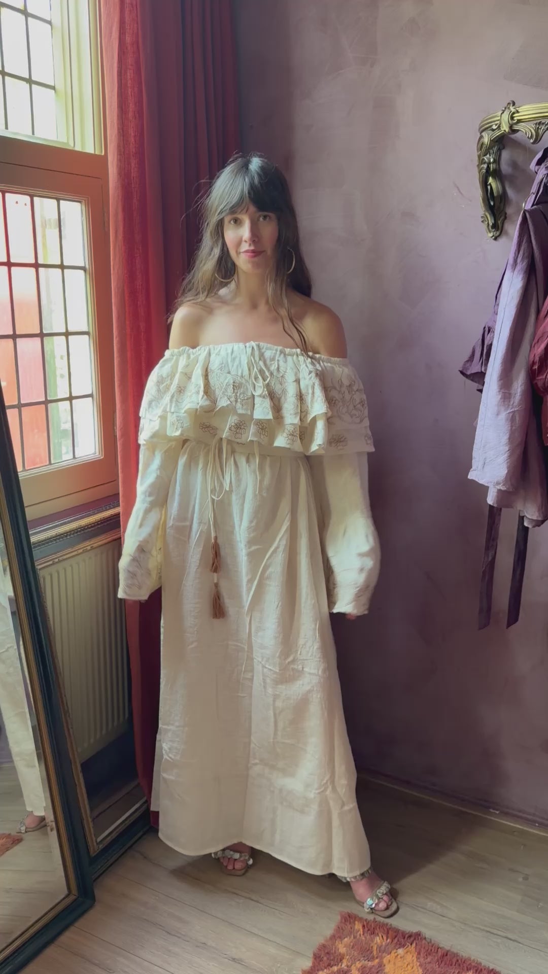 Cream khadi cotton bohemian maxi dress with bird embroidery, off-shoulder ruffle neckline, flowing bell sleeves, and tie waist belt.